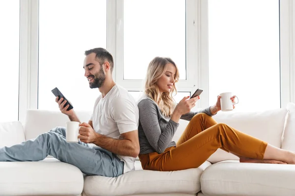 Милая любящая пара в помещении дома с помощью мобильных телефонов . — стоковое фото