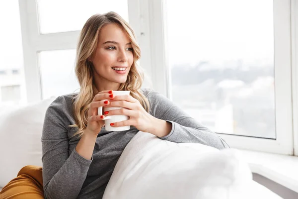 Bonita mulher bonita sentada dentro de casa segurando xícara beber chá . — Fotografia de Stock