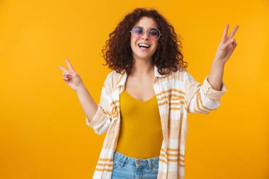 Güzel genç kıvırcık kız güneş gözlüğü takıyor sarı duvar arka plan üzerinde izole poz.