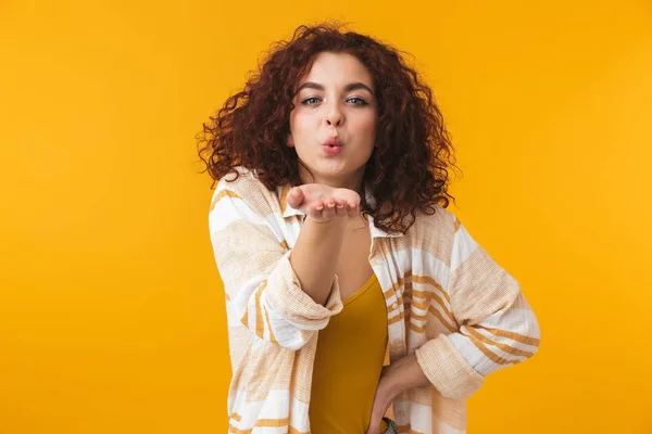 Hermosa joven rizado chica posando aislado sobre amarillo pared fondo soplando besos . — Foto de Stock