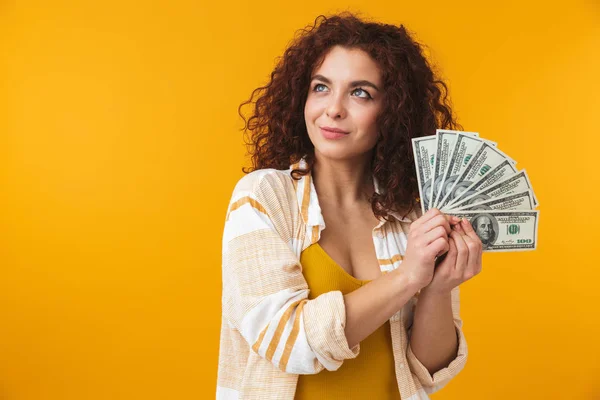 Schöne emotionale junge lockige Mädchen posiert isoliert über gelbe Wand Hintergrund hält Geld. — Stockfoto