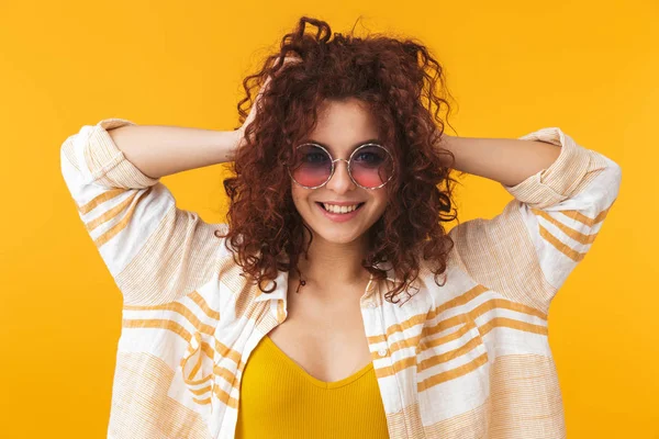 Belle jeune fille bouclée posant isolée sur fond de mur jaune portant des lunettes de soleil . — Photo