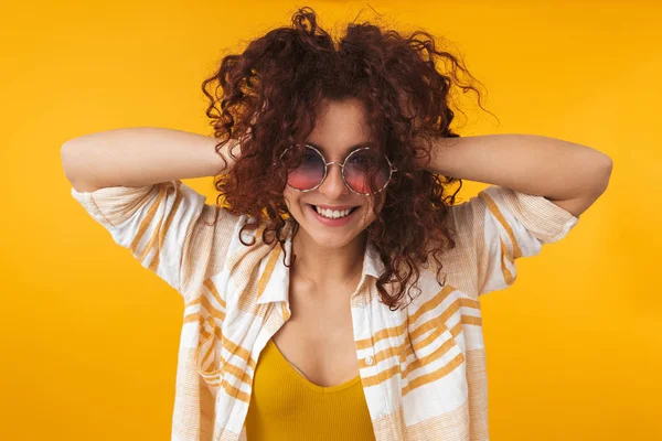 Beautiful young curly girl posing isolated over yellow wall background wearing sunglasses. — Stock Photo, Image