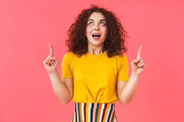 Mooie gekrulde meisje poseren geïsoleerde over rode muur achtergrond wijzen. — Stockfoto