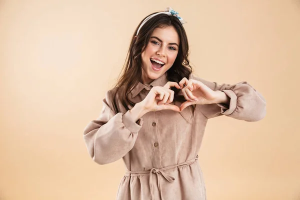 Linda joven posando aislada sobre fondo de pared beige mostrando gesto del corazón . —  Fotos de Stock