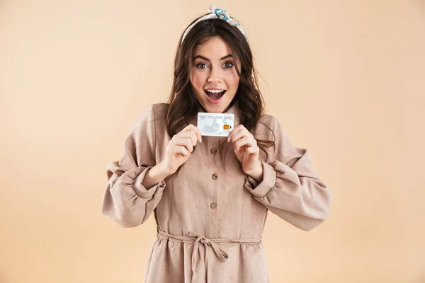 Enthousiast jonge mooie vrouw poseren geïsoleerde over beige achtergrond muur creditcard bedrijf. — Stockfoto