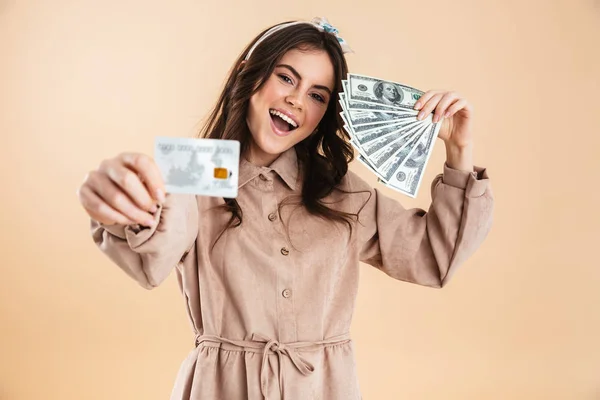 Mooie enthousiast jonge mooie vrouw poseren geïsoleerde over beige achtergrond muur holding creditcard en geld. — Stockfoto