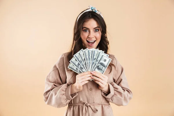 Mooie enthousiast jonge mooie vrouw poseren geïsoleerde over beige achtergrond muur aanhouden van geld. — Stockfoto