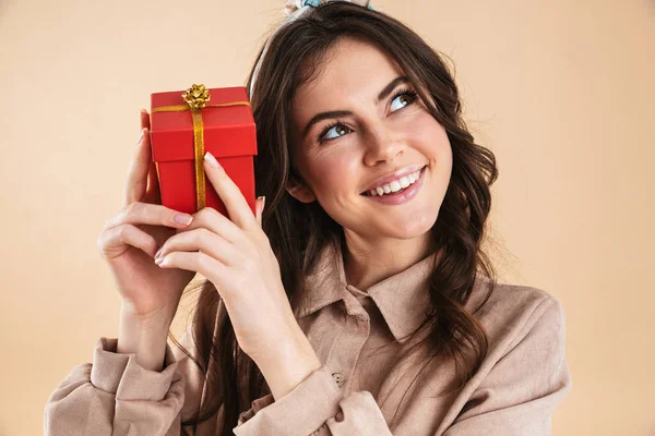 Aufgeregte junge hübsche Frau posiert isoliert über beige Hintergrundwand mit Geschenk-Box. — Stockfoto