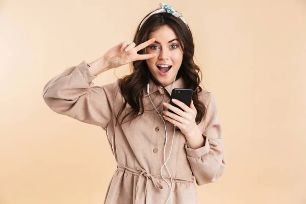 Mujer joven posando aislada sobre fondo de pared beige escuchando música con auriculares . — Foto de Stock