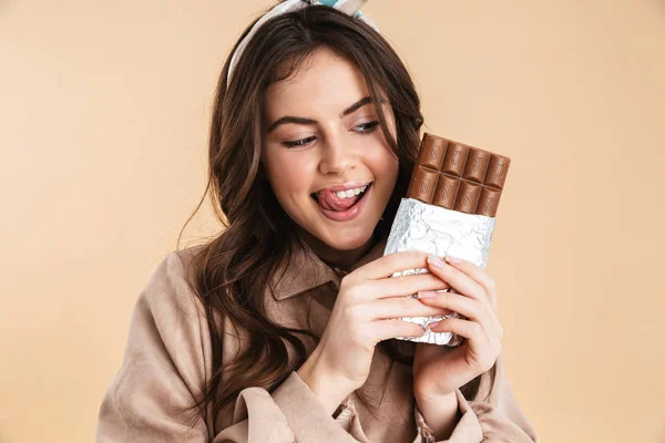 Excitada jovem bonita mulher posando isolado sobre fundo bege parede segurando chocolate . — Fotografia de Stock