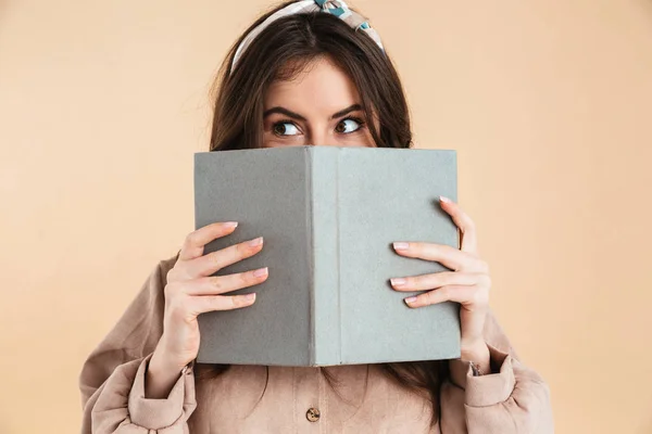 Jonge mooie vrouw poseren geïsoleerde over beige achtergrond muur holding boek lezen. — Stockfoto