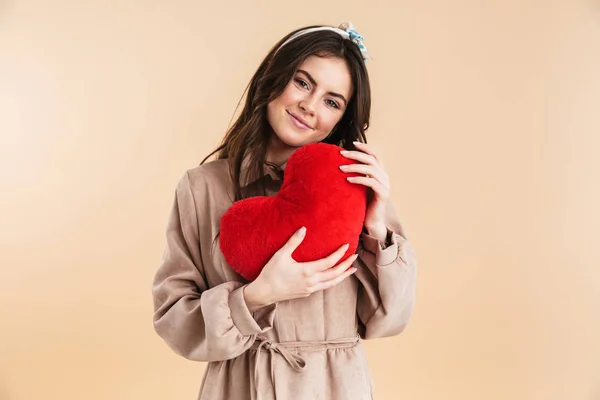 Jonge mooie vrouw poseren geïsoleerde over beige achtergrond muur houdt hart speelgoed. — Stockfoto