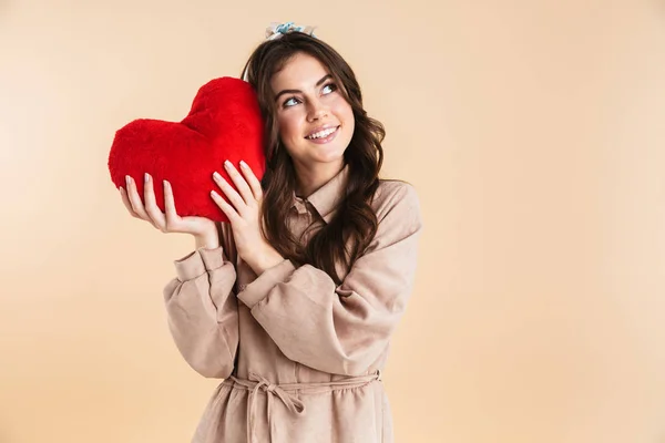 Junge hübsche Frau posiert isoliert über beigem Hintergrund Wand hält Herz Spielzeug. — Stockfoto