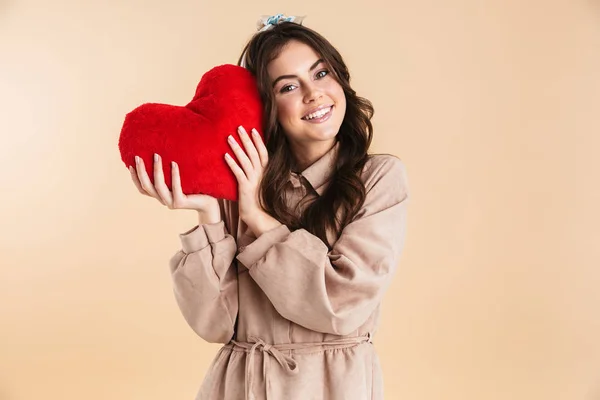 Young pretty woman posing isolated over beige background wall holding heart toy. — Stock Photo, Image