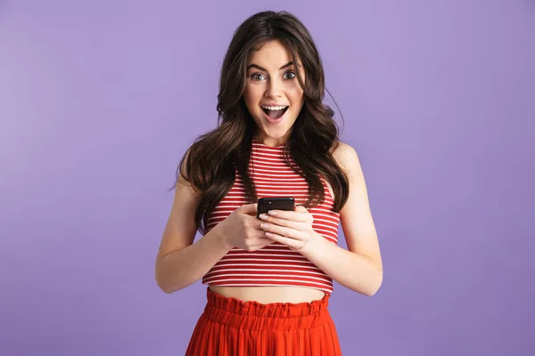 Impresionado joven mujer bonita emocionada posando aislado sobre la pared de fondo púrpura utilizando el teléfono móvil . —  Fotos de Stock