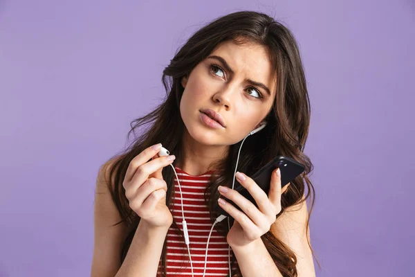 Mujer bonita joven reflexiva posando aislada sobre la pared de fondo púrpura escuchando música con auriculares . — Foto de Stock