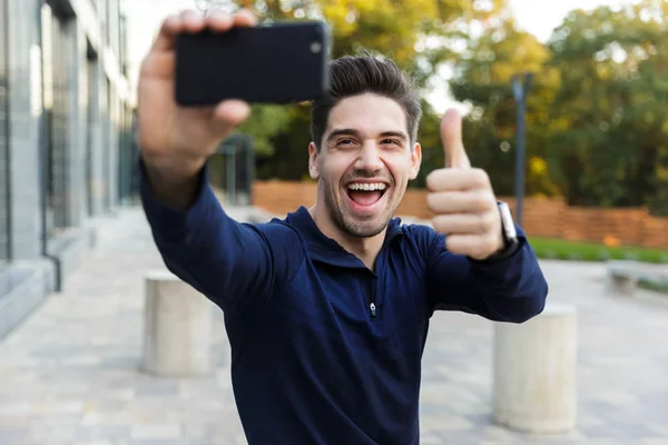 Sorridente giovane sportivo prendendo un selfie mentre seduto — Foto Stock