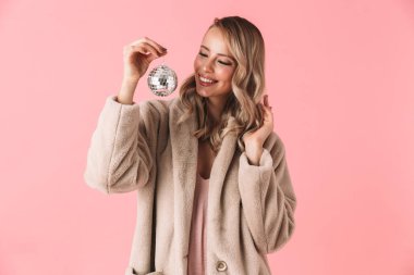 Kadın küçük disko topu tutan moda ceket giymiş pembe duvar arka plan üzerinde izole poz.