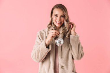 Kadın küçük disko topu tutan moda ceket giymiş pembe duvar arka plan üzerinde izole poz.