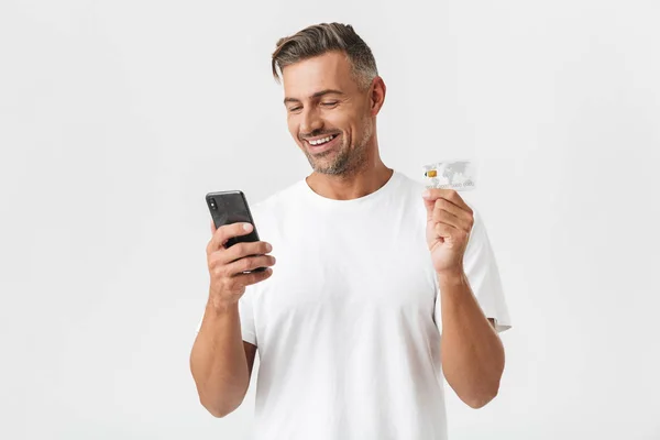 Imagen del hombre feliz de 30 años usando una camiseta casual sosteniendo un teléfono inteligente — Foto de Stock