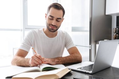 Evde dizüstü bilgisayar üzerinde çalışan yakışıklı genç adam