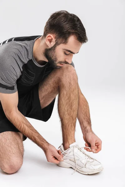 Jovens esportes fitness homem corredor posando isolado sobre fundo da parede branca amarrar seus atacadores . — Fotografia de Stock