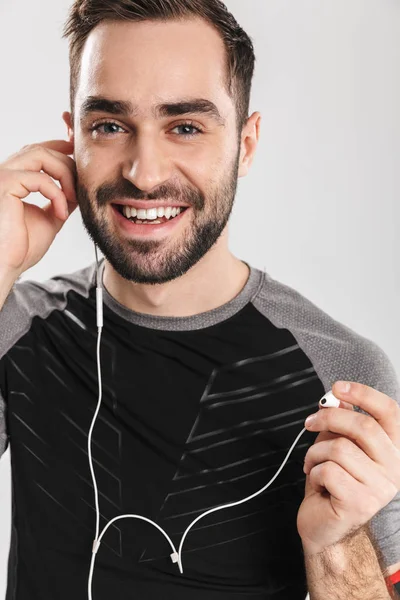 Όμορφος νέος αθλητισμός Fitness άνθρωπος που θέτει απομόνωση πάνω από το λευκό τοίχωμα φόντο ακούγοντας μουσική με ακουστικά. — Φωτογραφία Αρχείου