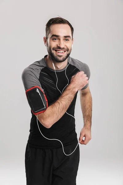 Bonito jovem esportes fitness homem posando isolar sobre fundo da parede branca ouvir música com fones de ouvido . — Fotografia de Stock