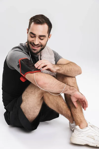 Guapo joven deportista fitness hombre posando aislado sobre fondo blanco de la pared escuchando música con auriculares . — Foto de Stock