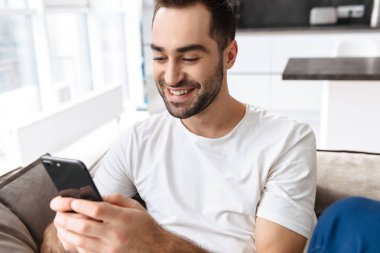 Evde bir kanepede oturan gülümseyen genç adam