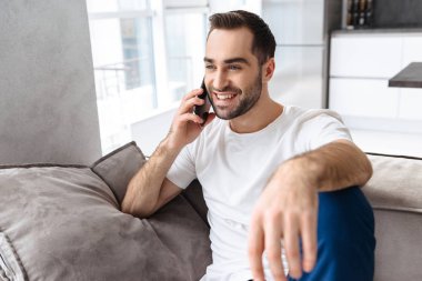 Evde bir kanepede oturan gülümseyen genç adam