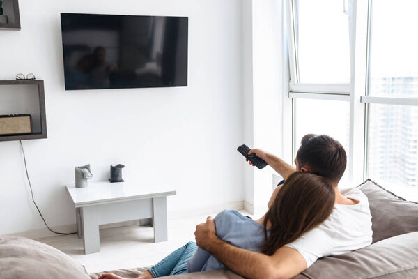 Image from back of attractive couple in casual wear watching tel