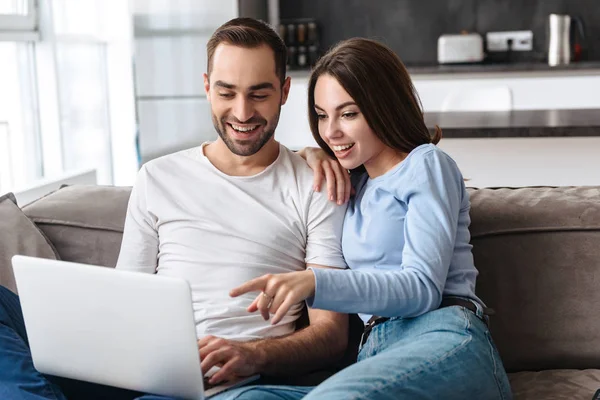 Imagen de pareja feliz usando el ordenador portátil juntos mientras están sentados en sof — Foto de Stock