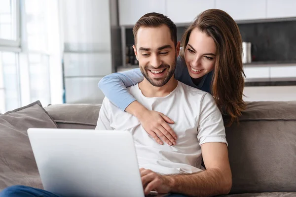 Image of joyful couple using laptop together while sitting on so — Stock Photo, Image