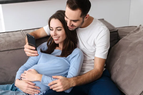 Imagen de una mujer embarazada positiva y un hombre guapo acostado en el sofá — Foto de Stock