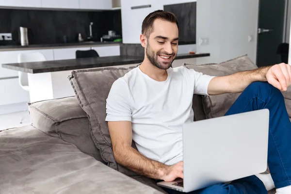 Jovem sorridente sentado em um sofá em casa — Fotografia de Stock