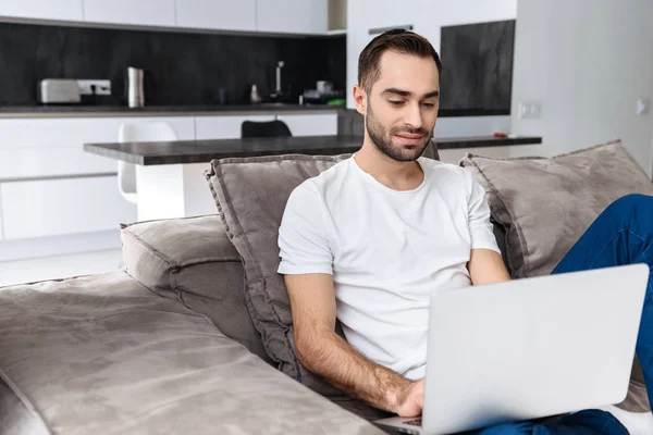 Lächelnder junger Mann sitzt zu Hause auf einer Couch — Stockfoto