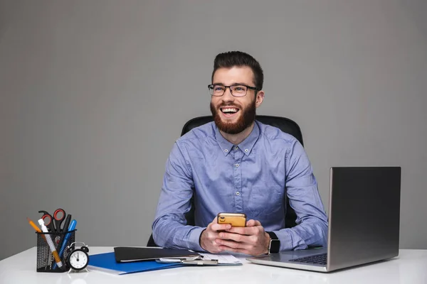 Allegro uomo elegante barbuto in occhiali da vista seduto con smartphone — Foto Stock