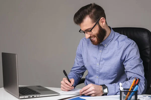 Smiling bearded elegant man in eyeglasses writing something — Stock Photo, Image