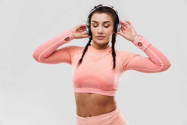 Erstaunliche starke Sport Fitness Frau posiert isoliert über weiße Wand Hintergrund Musik hören mit Kopfhörern. — Stockfoto