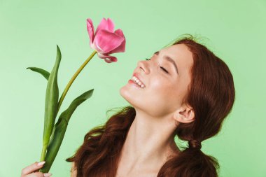 Mutlu genç kızıl saçlı kız çiçek tutan yeşil duvar arka plan üzerinde izole poz.