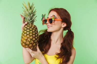 Mutlu genç kızıl saçlı kız ananas tutan yeşil duvar arka plan üzerinde izole poz.