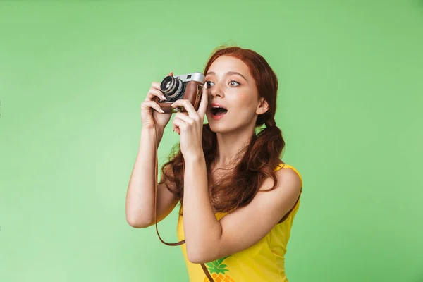 Jovem fotógrafo menina ruiva feliz posando isolado sobre fundo parede verde segurando câmera . — Fotografia de Stock