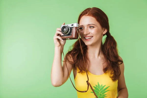 행복 한 젊은 빨강 머리 소녀 사진 작가 포즈 고립 위에 녹색 벽 배경 들고 카메라. — 스톡 사진
