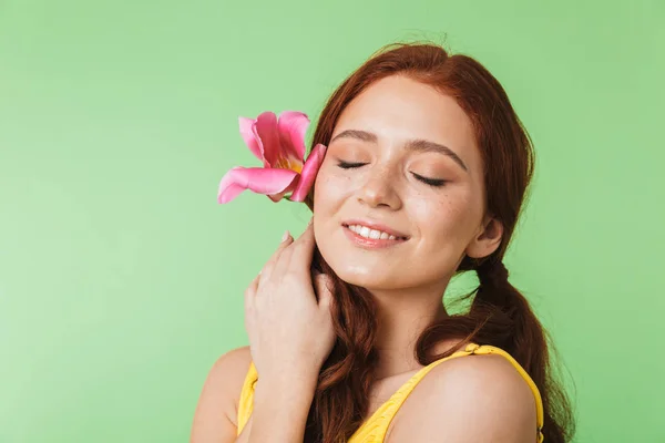 Happy young redhead girl posing isolated over green wall background holding flower. — Stock Photo, Image
