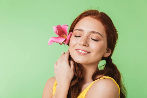 Feliz joven pelirroja posando aislada sobre fondo de pared verde sosteniendo flor . —  Fotos de Stock