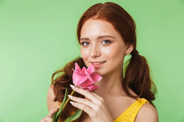 Happy young redhead girl posing isolated over green wall background holding flower. — Stock Photo, Image