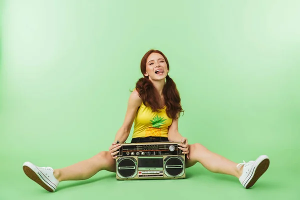 Lycklig ung rödhårig flicka poserar isolerade över grön vägg bakgrund med Boombox. — Stockfoto