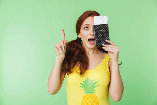 Hermosa chica pelirroja sorprendida posando aislada sobre fondo de pared verde con pasaporte y boletos . — Foto de Stock